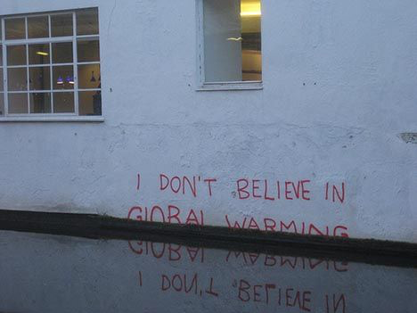 a flooded street with grafitti on a wall that is reflected in the water that reads I DONT BELIEVE IN GLOBAL WARMING